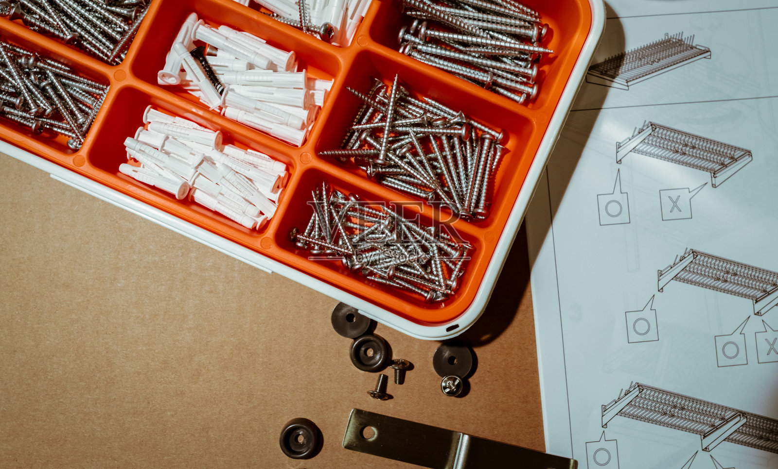 螺丝和墙壁插头插在橙色塑料盒里。俯视图工具盒在棕色的背景与盘子干燥架组装说明。一套螺钉和塑料塞钻墙和安装东西。照片摄影图片