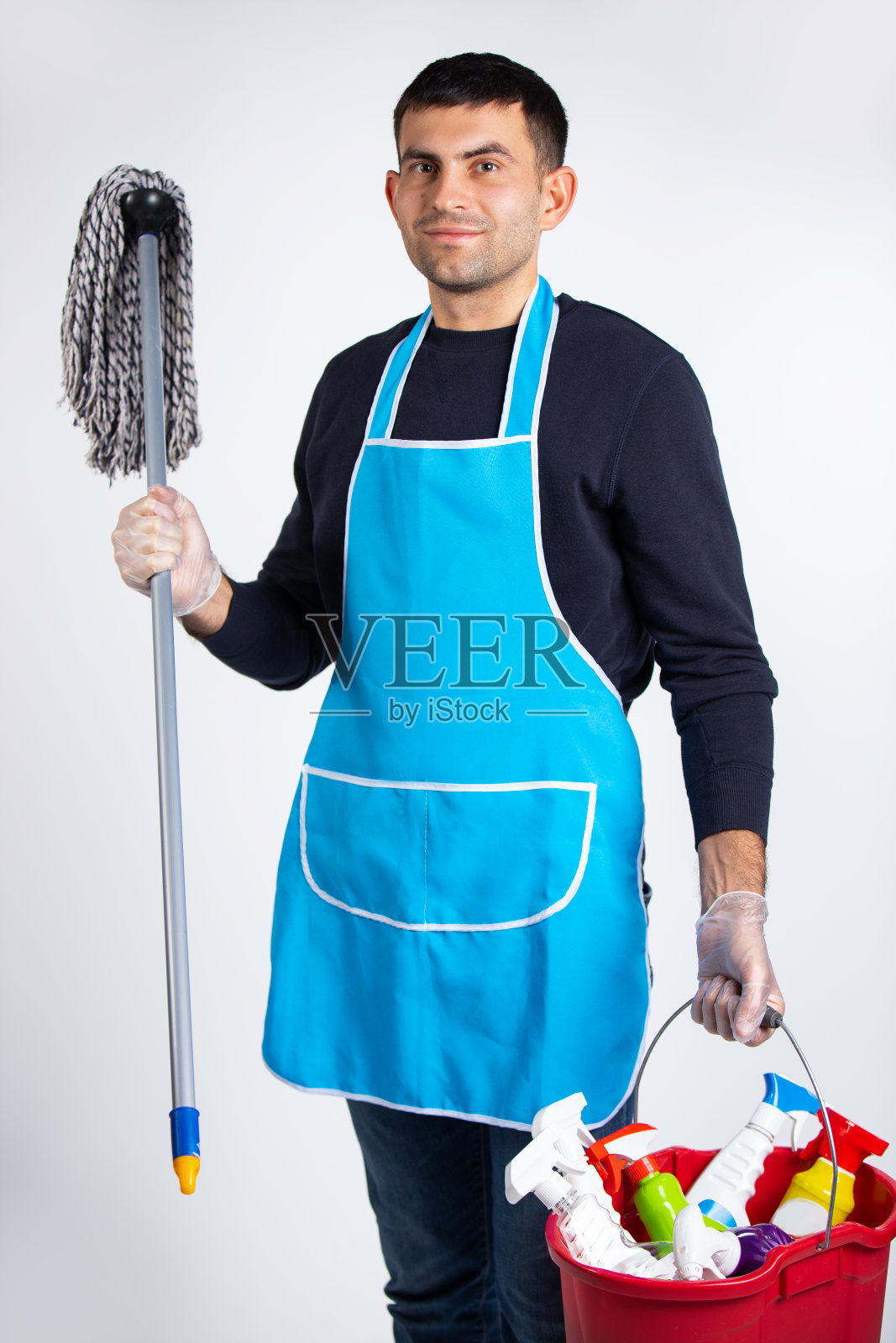 性别刻板印象，男人戴着手套，穿着长袍，用化学品打扫房间。白色背景上的照片。清洁和清洁概念照片摄影图片