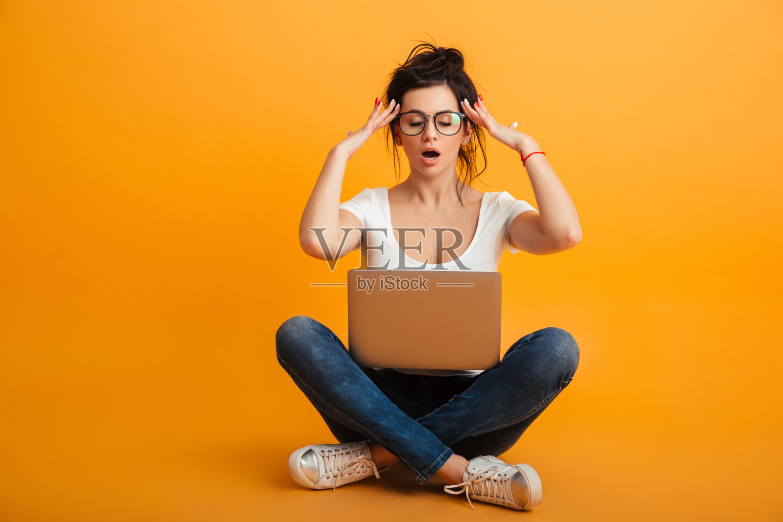 一个严肃的女人，穿着便服，戴着眼镜，闭着眼睛，双腿交叉坐在地板上，越过黄色的墙，触摸太阳鬓照片摄影图片