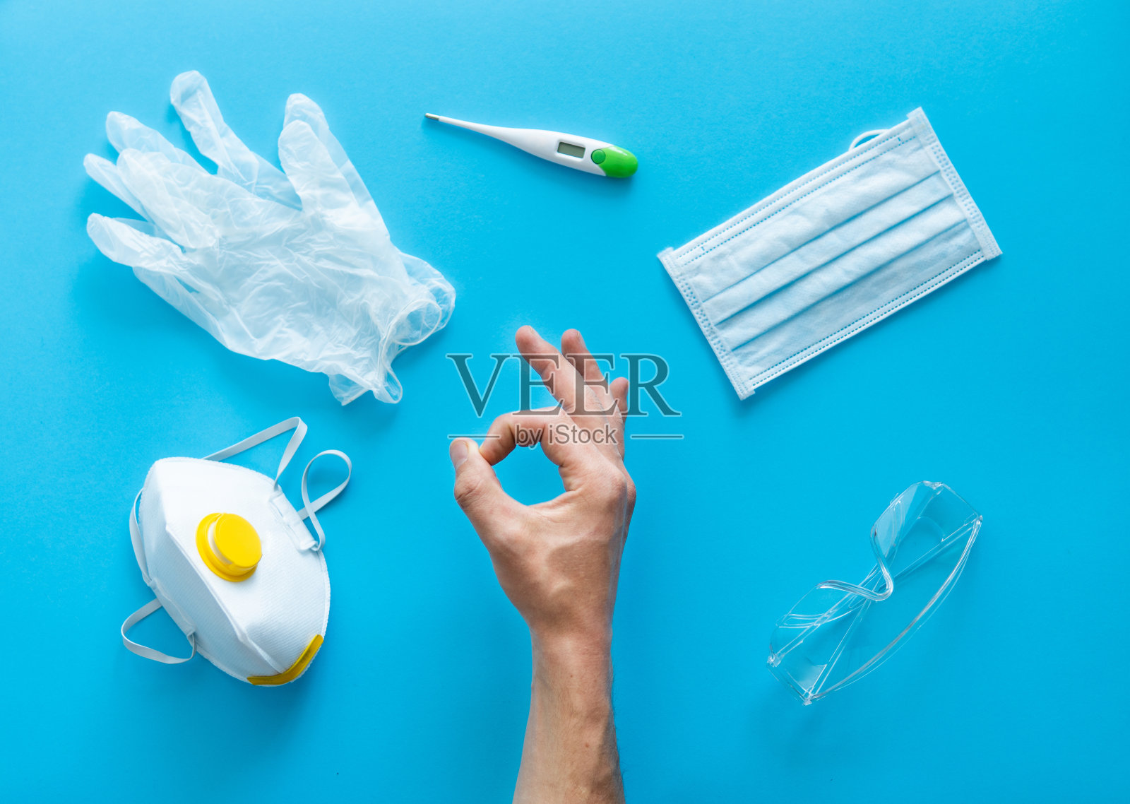 佩戴医用防护口罩、呼吸器、橡胶手套、体温计和防护眼镜的男子的手显示ok。2019年冠状病毒大流行。照片摄影图片