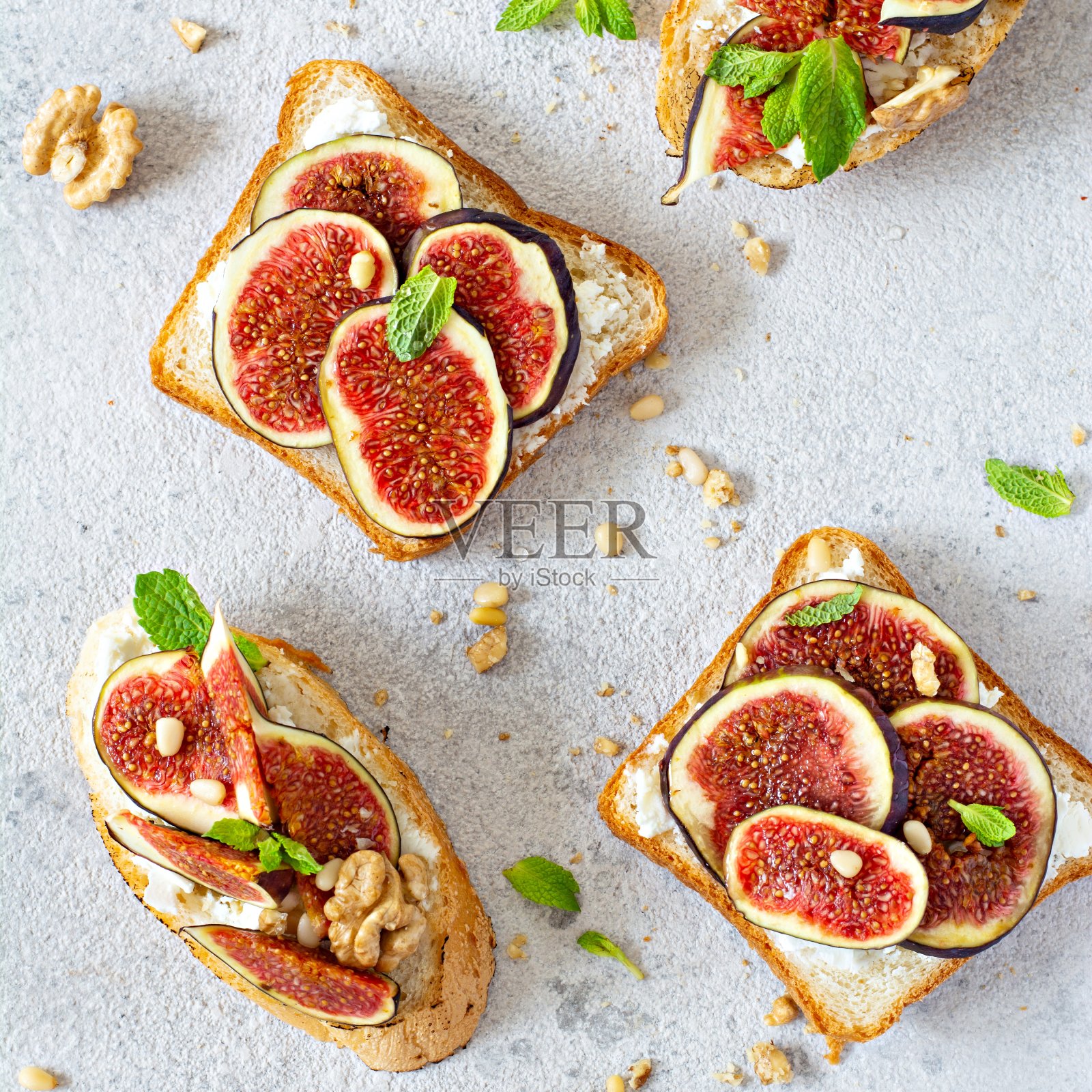 脆脆的意式烤面包配上松软的意大利乳清干酪、成熟的无花果、核桃和松子、薄荷和蜂蜜。大理石桌上的无花果吐司配蜂蜜和核桃。前视图。照片摄影图片