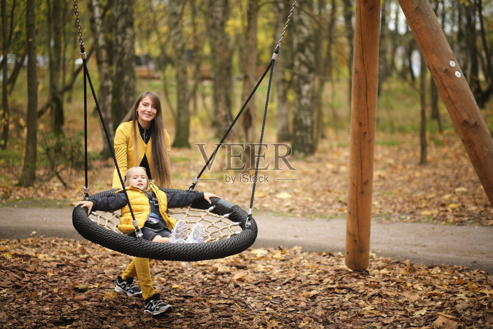 那位年轻妇女在荡秋千带她的小女儿。妈妈和女儿在一起很开心。秋季时尚照片摄影图片