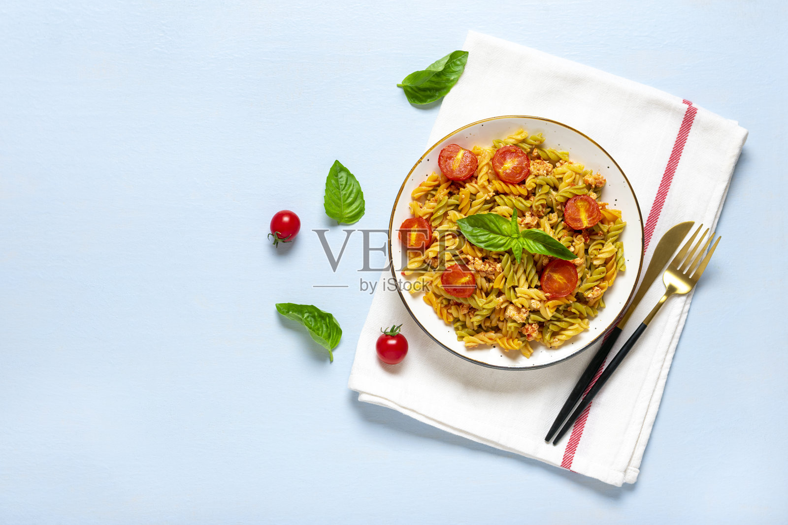 经典的意大利面食，由硬质小麦与鸡肉，西红柿，樱桃，罗勒番茄酱在白色的碗，餐巾，叉子在蓝色的木桌地中海美食照片摄影图片