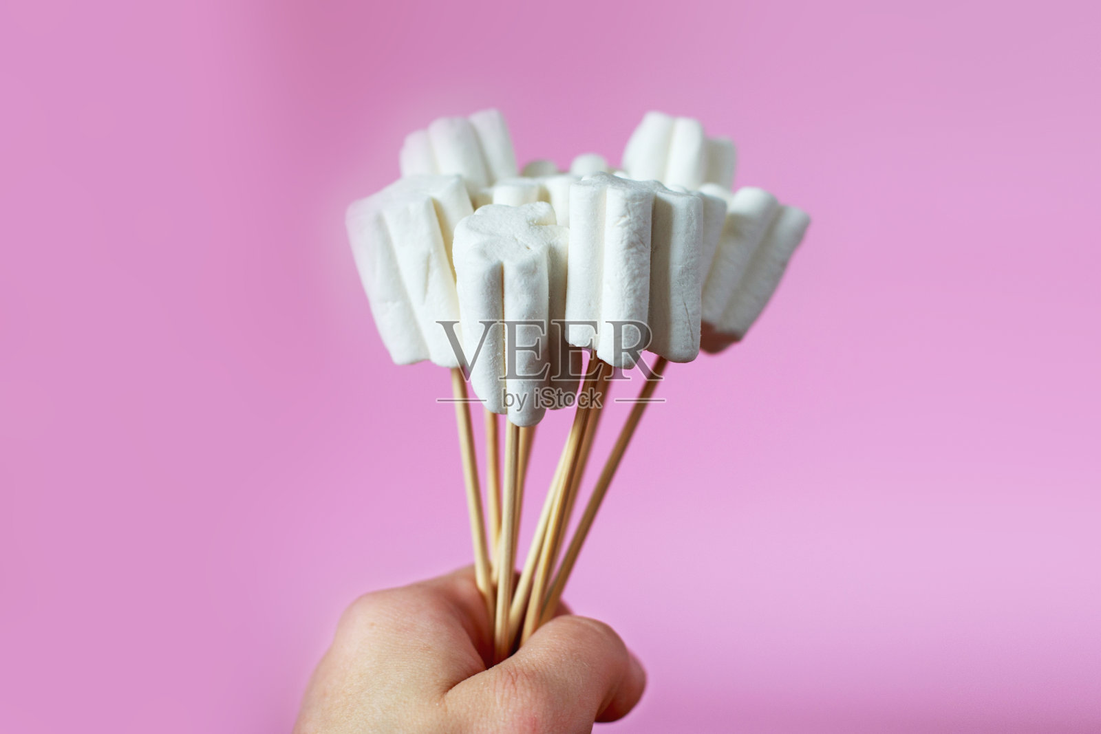 粉红色背景上的棉花糖花束。孩子的手拿着一束糖果照片摄影图片