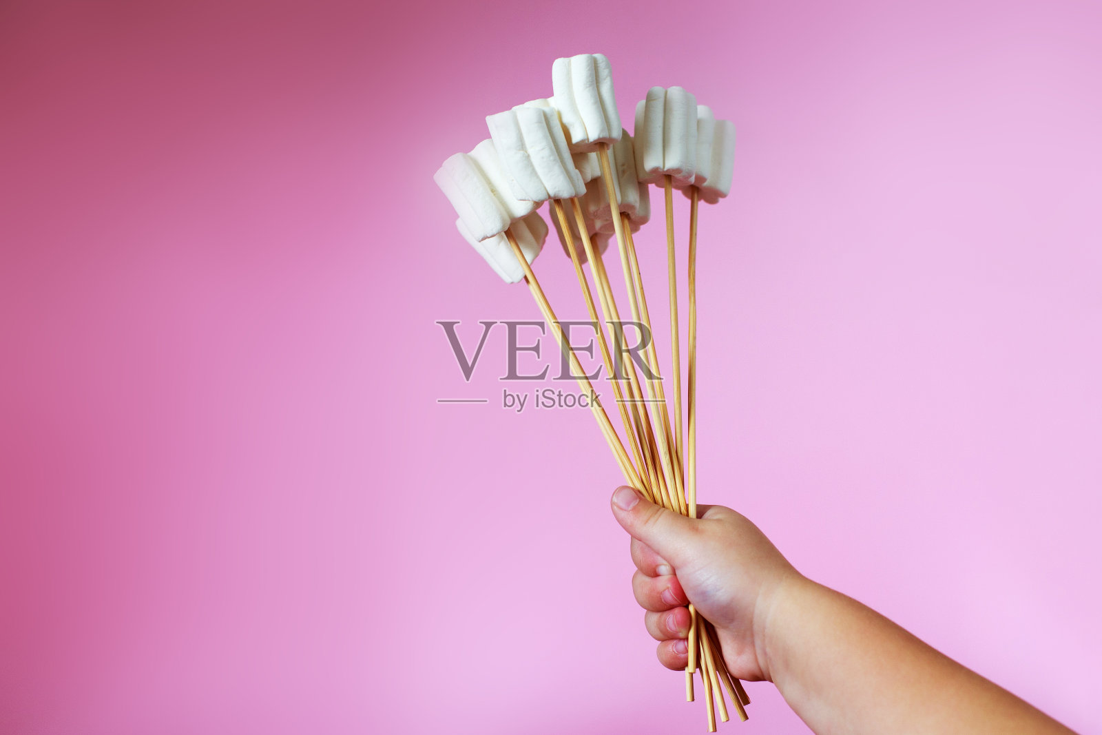 粉红色背景上的棉花糖花束。孩子的手拿着一束糖果照片摄影图片