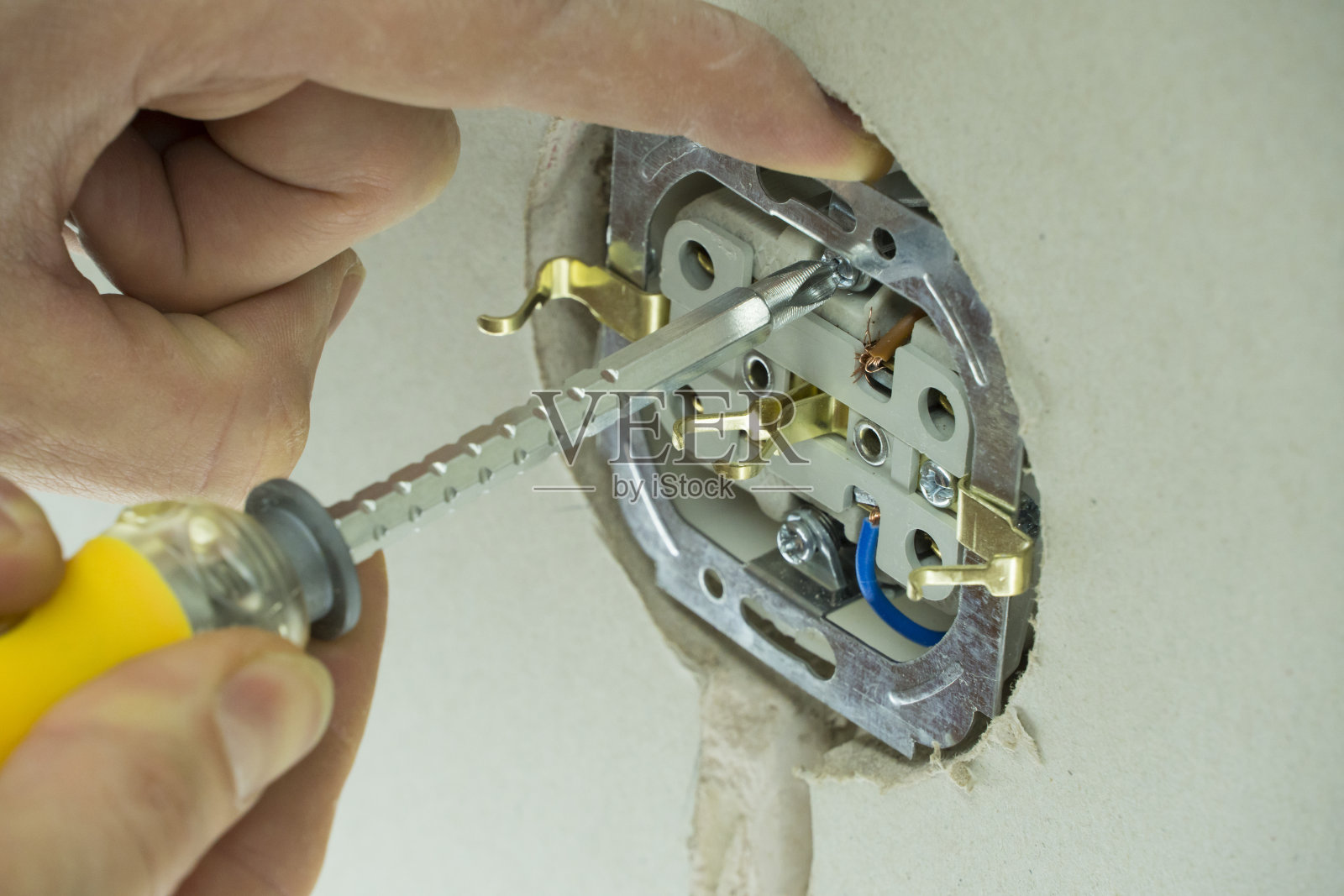 电工把插座接到电线上。将电线安装到插头上。一个男人在墙上安装了一个插座。关闭在电源插座附近拿着螺丝刀的技术人员。照片摄影图片