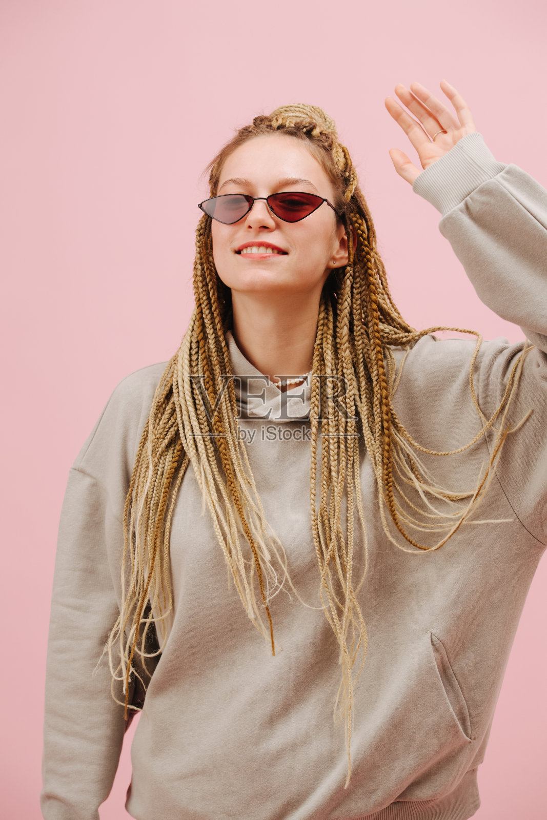 友好的女人戴着太阳镜，在粉红色的背景上梳着时髦的金发非洲式辫子照片摄影图片
