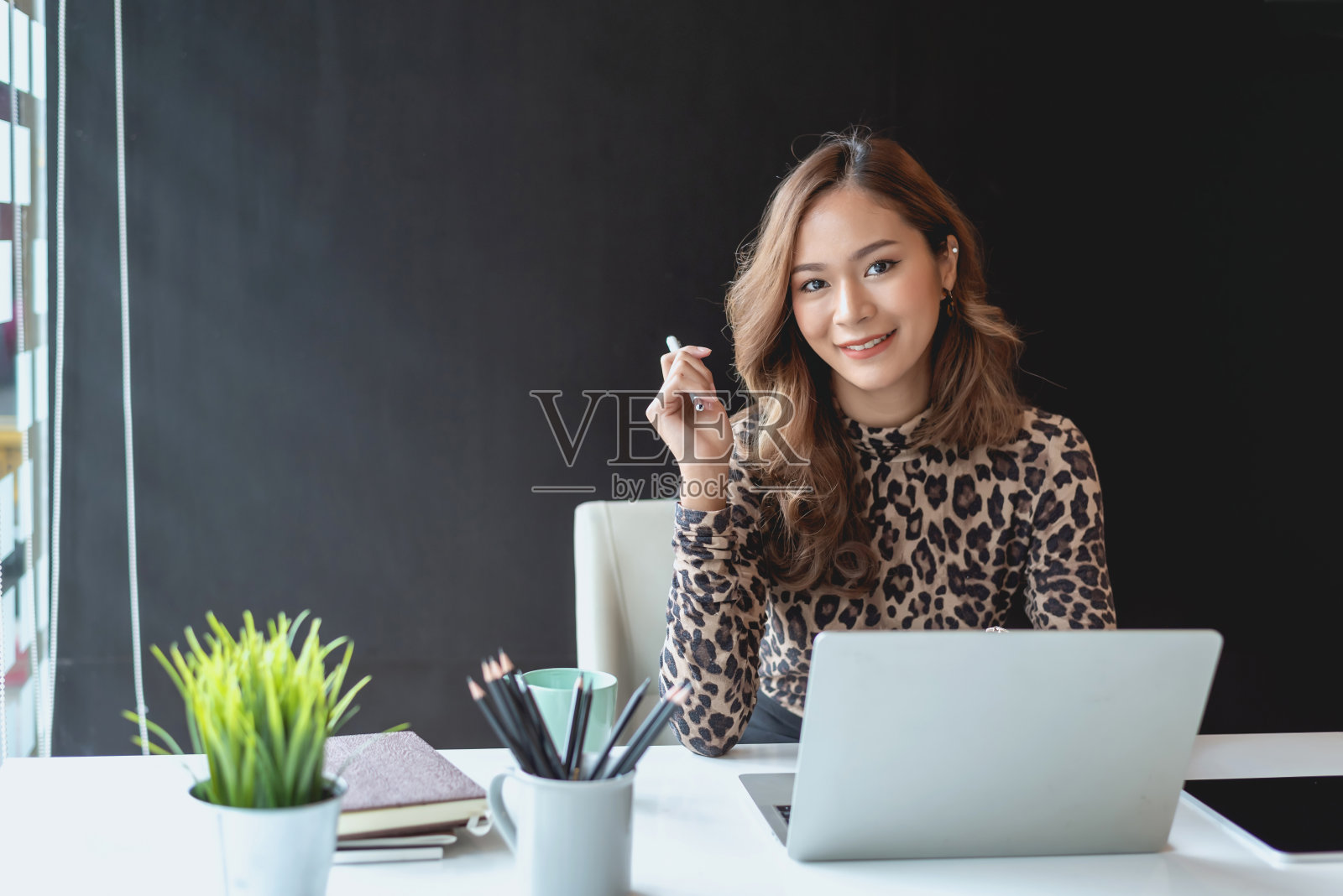 迷人的亚洲女商人坐在办公室里用笔记本电脑工作。看相机。照片摄影图片