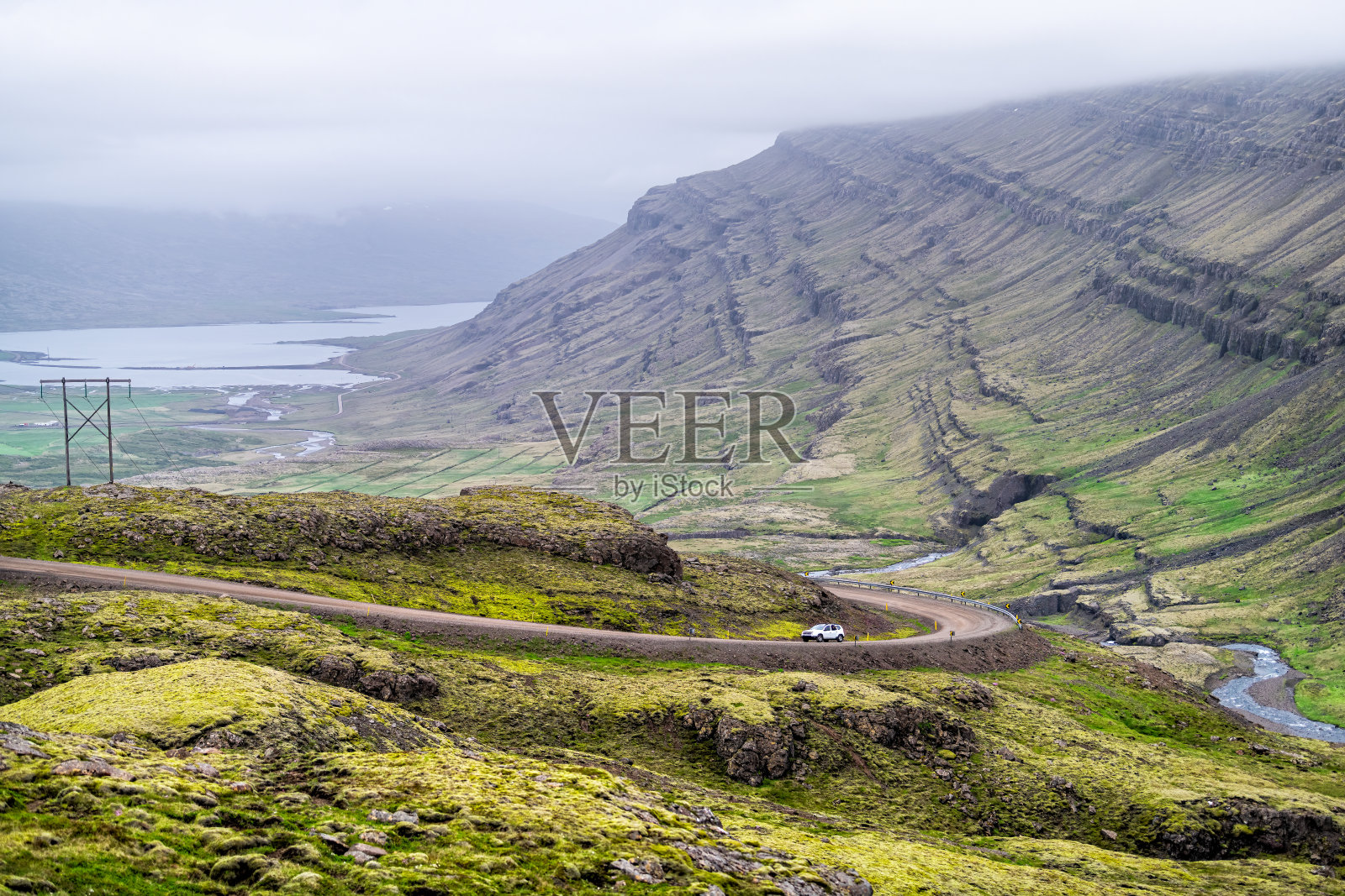 环岛公路1号线以东的冰岛高速公路上有青苔绿的景观山和汽车在陡峭的斜坡上，阴天多云的暴风雨天气在贝鲁约尔地区照片摄影图片
