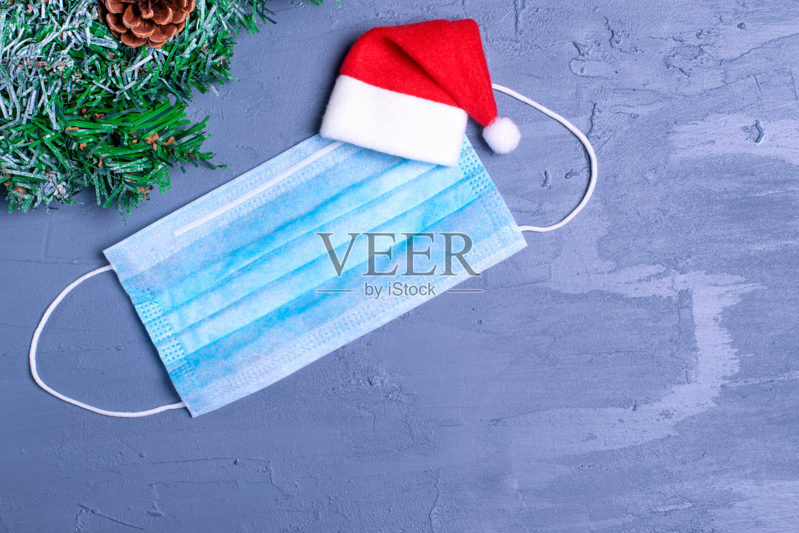 灰色背景下的一次性面具和圣诞老人帽。平安圣诞和新年庆祝的概念照片摄影图片