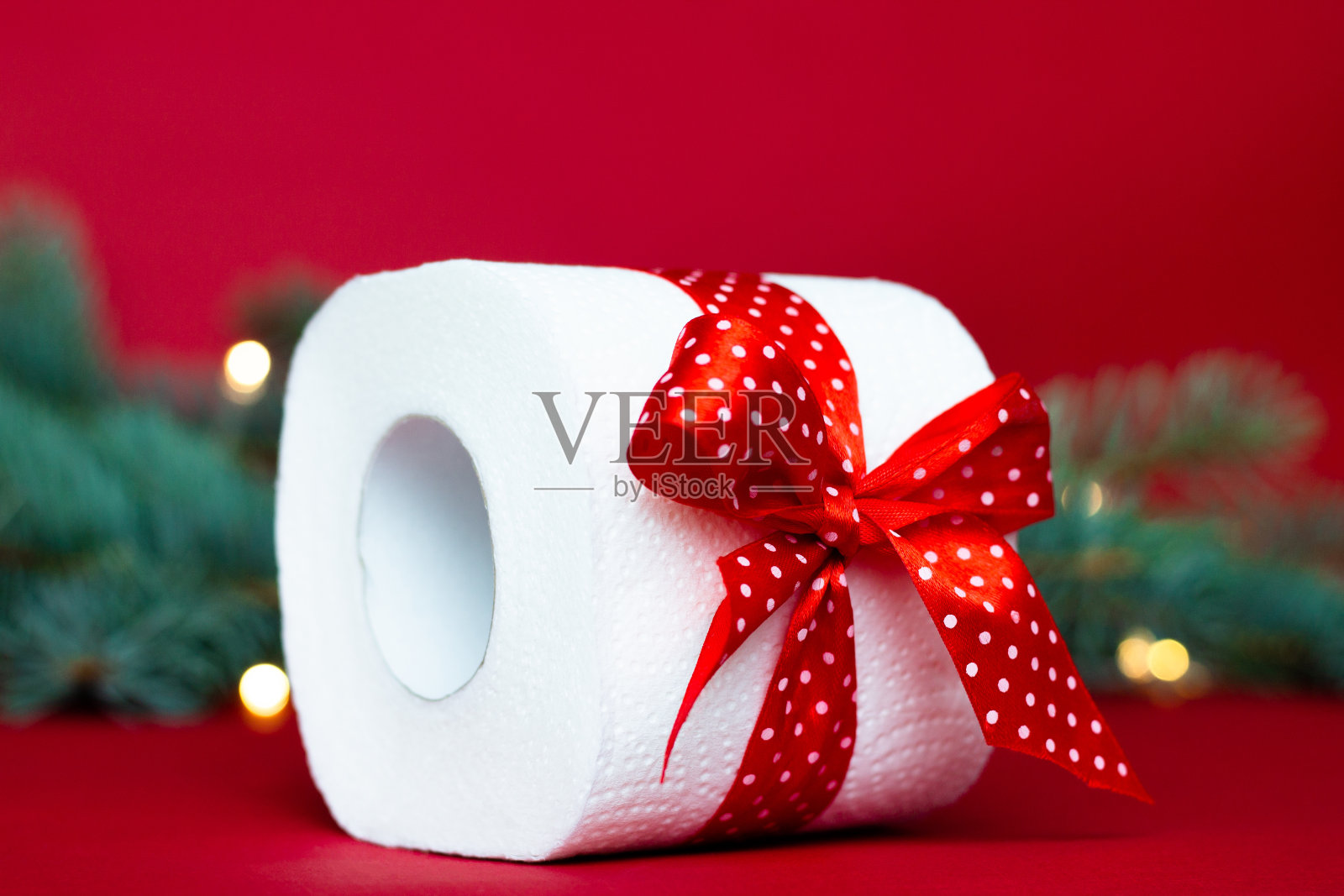 一卷卫生纸作为圣诞礼物放在红色背景的圣诞树树枝旁照片摄影图片
