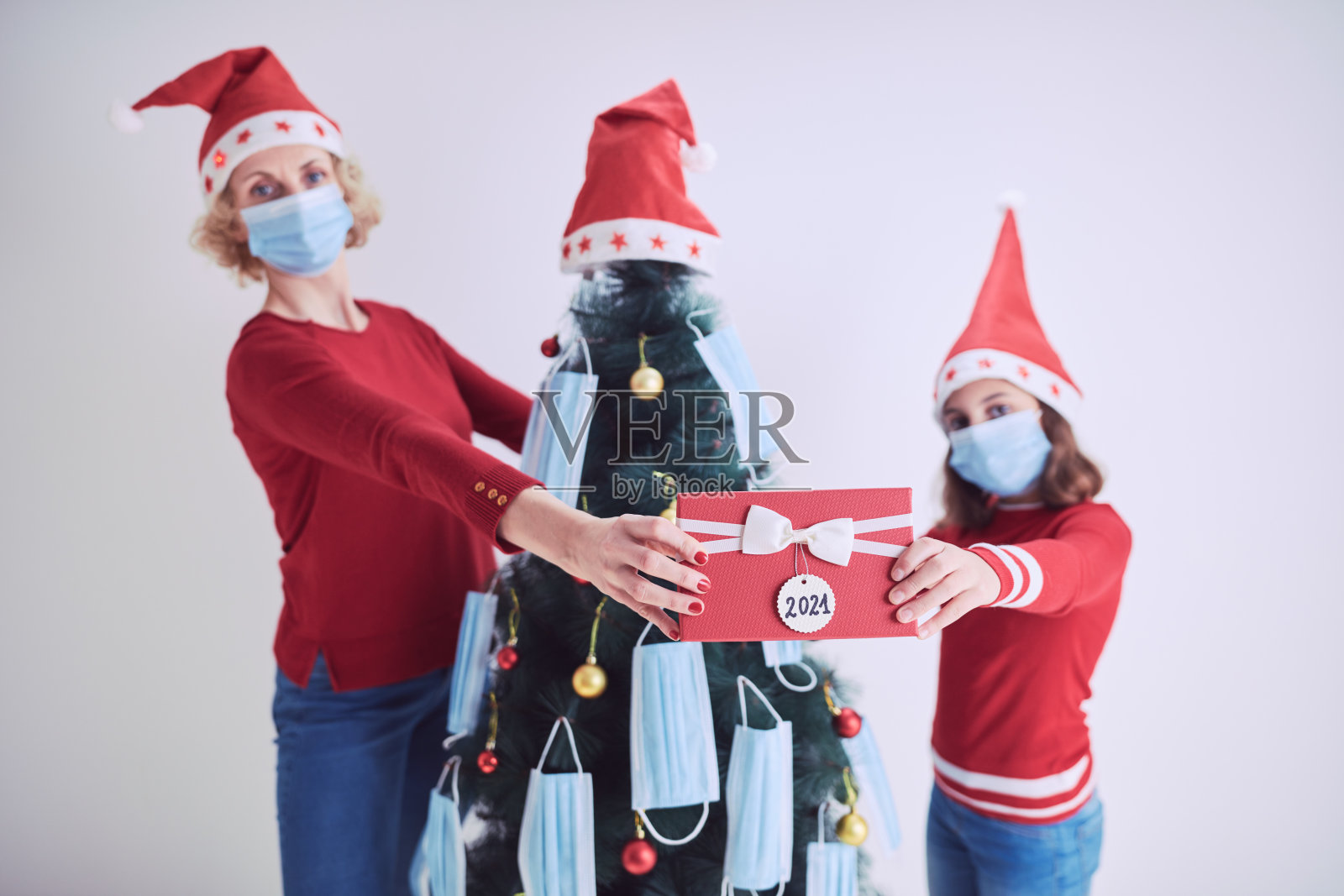 在2020/2021年病毒大流行期间，母亲和女儿用医用口罩装饰圣诞树。照片摄影图片