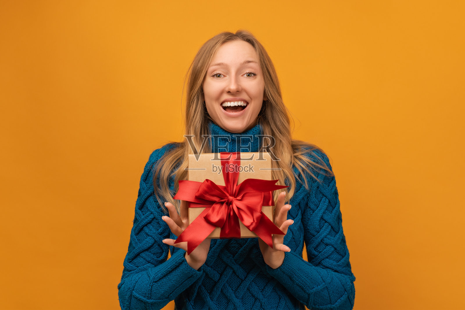 一个快乐的年轻女子的肖像拿着用丝带装饰的礼物。工作室拍摄，黄色背景照片摄影图片