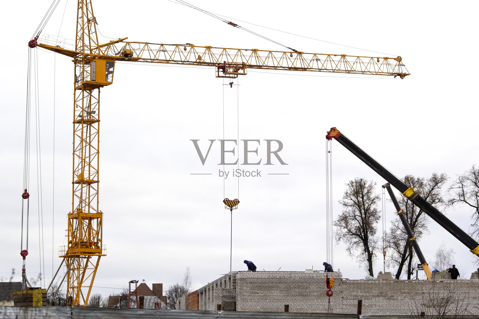 在冬季多云的天空背景下，几台建筑起重机。起重机和建筑工程。大的黄色的起重机。建筑的概念。互联网网站。照片摄影图片