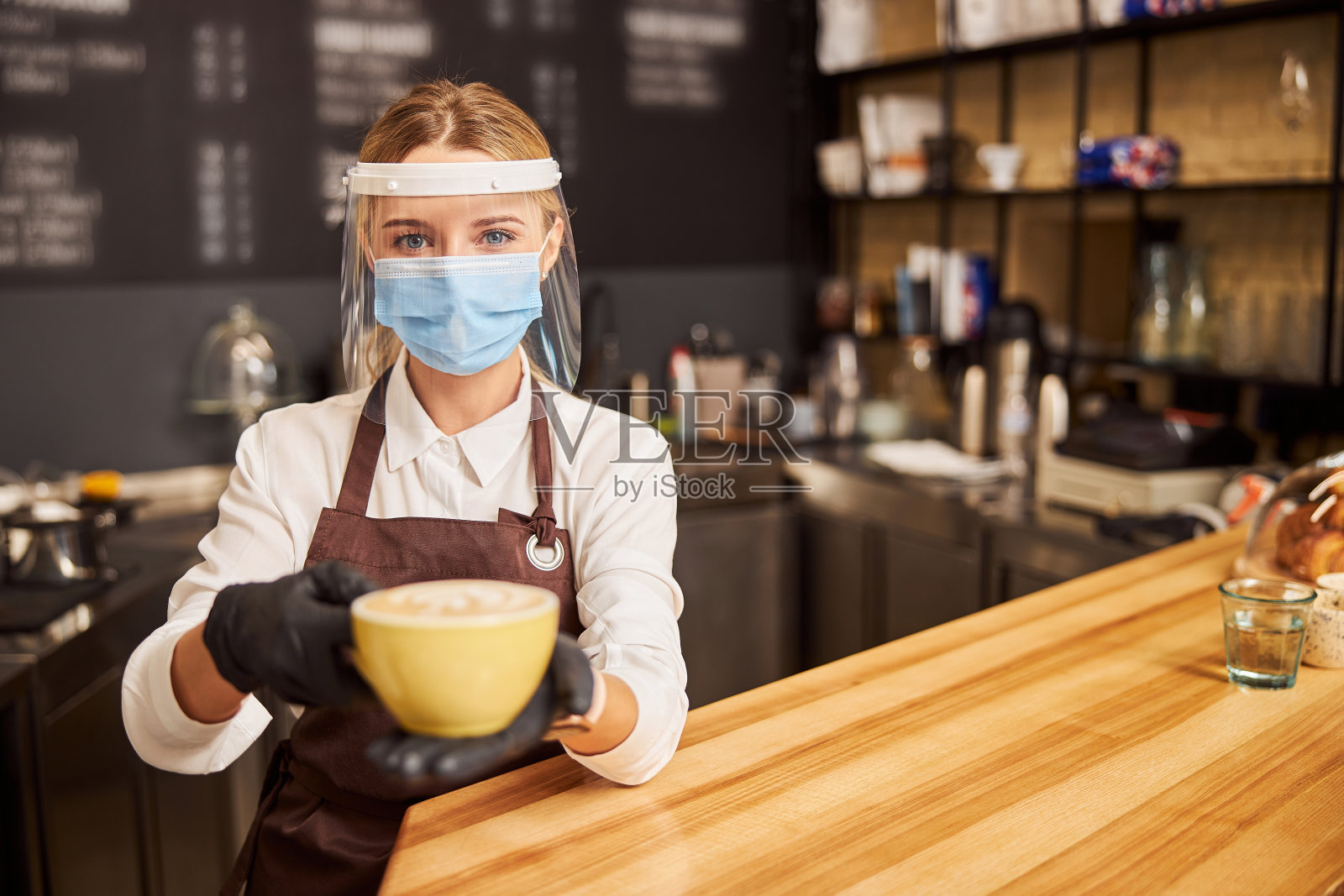 漂亮的咖啡师，手里拿着一杯热卡布奇诺照片摄影图片