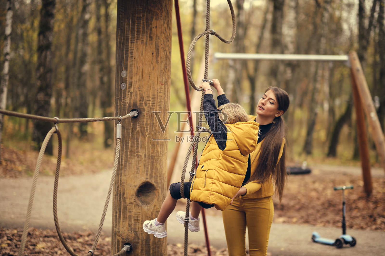 美丽的小女孩爬上了绳索公园。运动装现代勇敢的女孩。妈妈和女儿在一起很开心。秋季时尚照片摄影图片