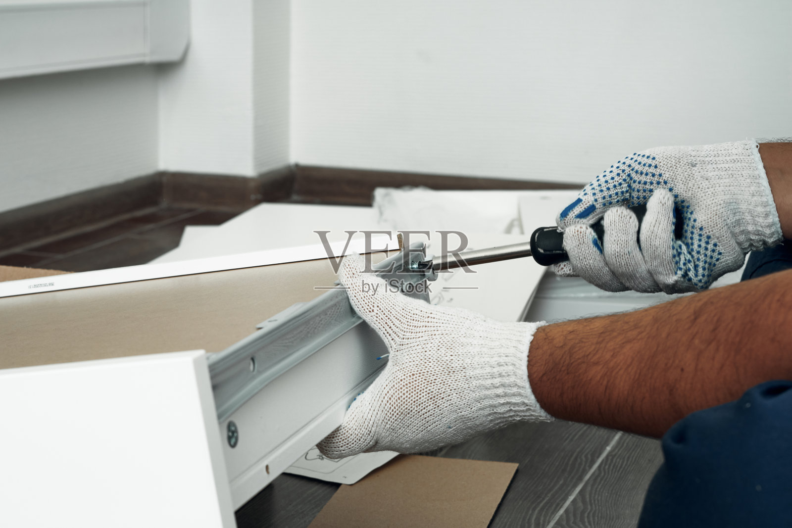 家具组装过程。穿着工装裤和白色鞋的工人。使用螺丝刀。做你自己。照片摄影图片