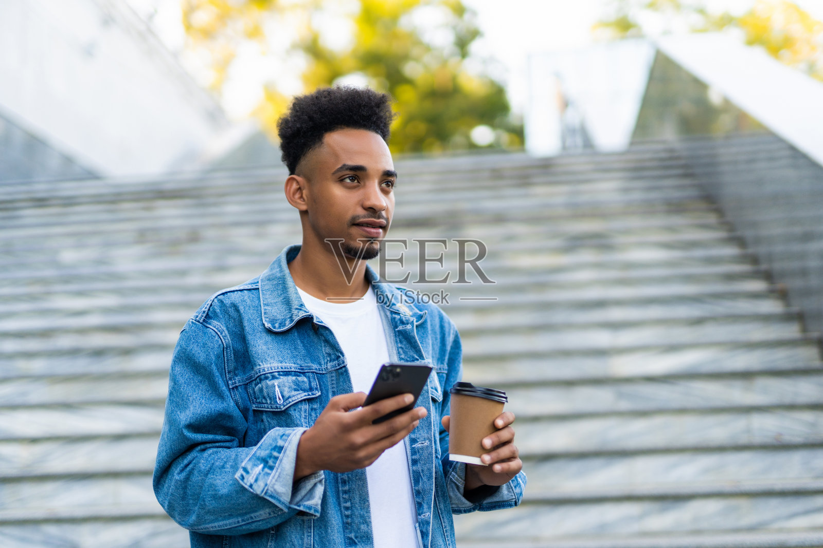 一幅非裔美国人在大街上拿着咖啡看手机的照片照片摄影图片