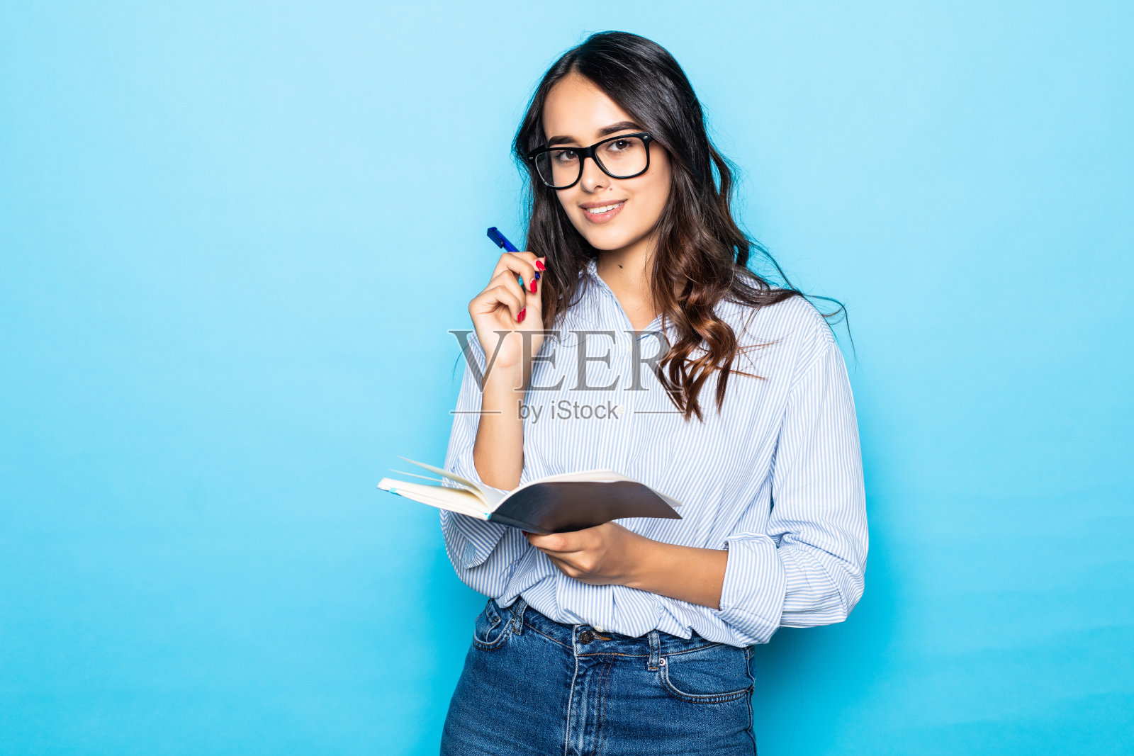 年轻的女孩买了新的记事本，写笔记或讲座，开心地微笑，拿着红色的笔记本，决定开始秘密日记，站在蓝色的背景照片摄影图片