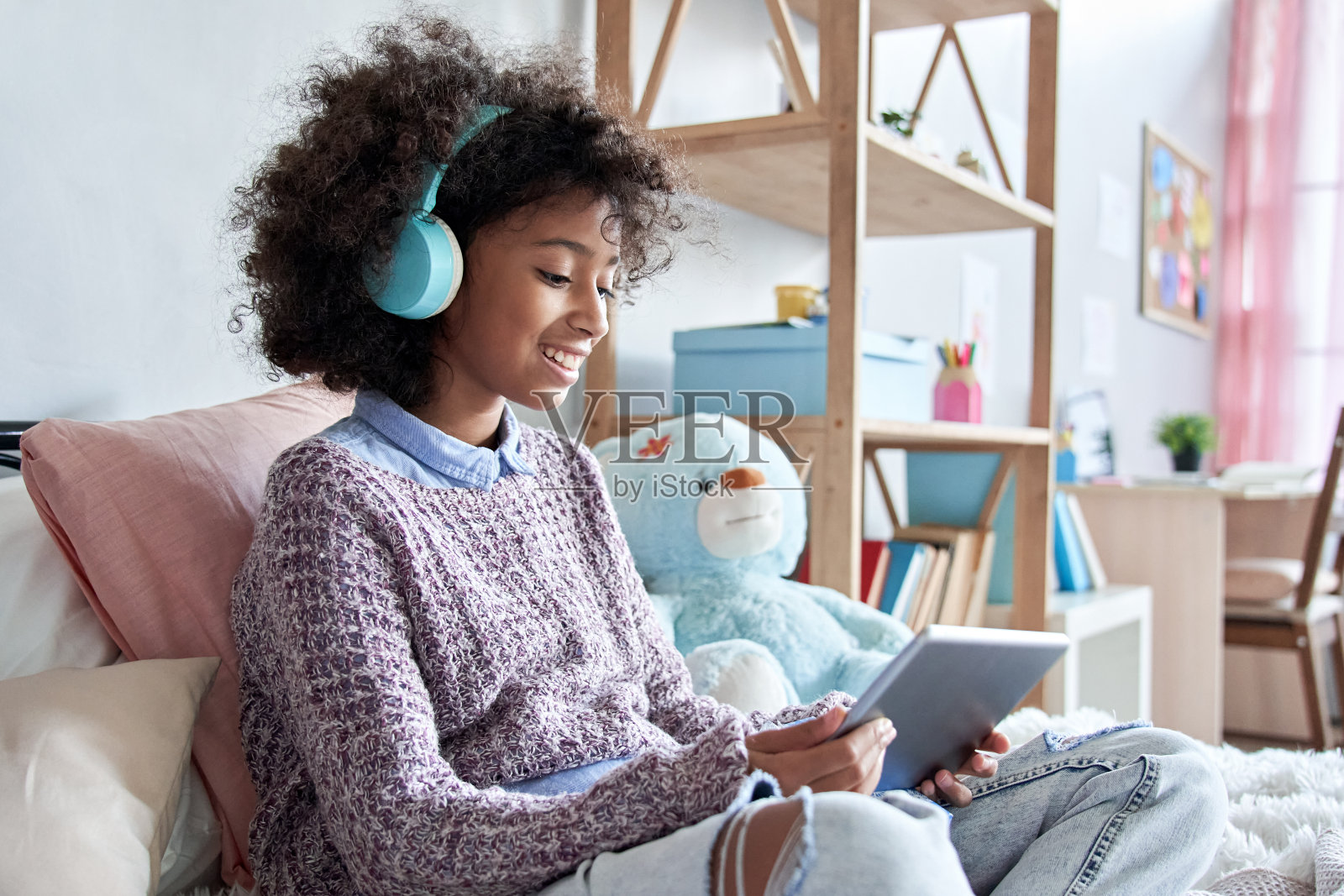 快乐的非洲小女孩拿着数字平板电脑在家学习。微笑的混合种族学校的孩子使用设备远程学习观看社交媒体视频虚拟课堂坐在床上在线。照片摄影图片