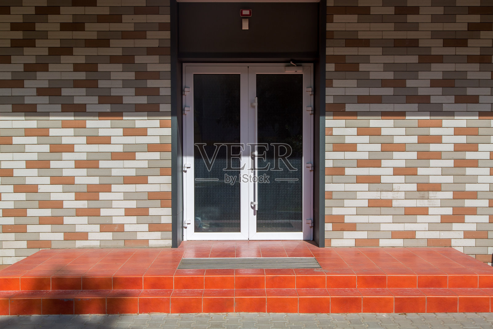 门槛上铺着红色的瓷砖和脚垫，前门是白色的带玻璃的砖墙建筑，在一个阳光明媚的日子里，走近台阶的入口，没有人。照片摄影图片