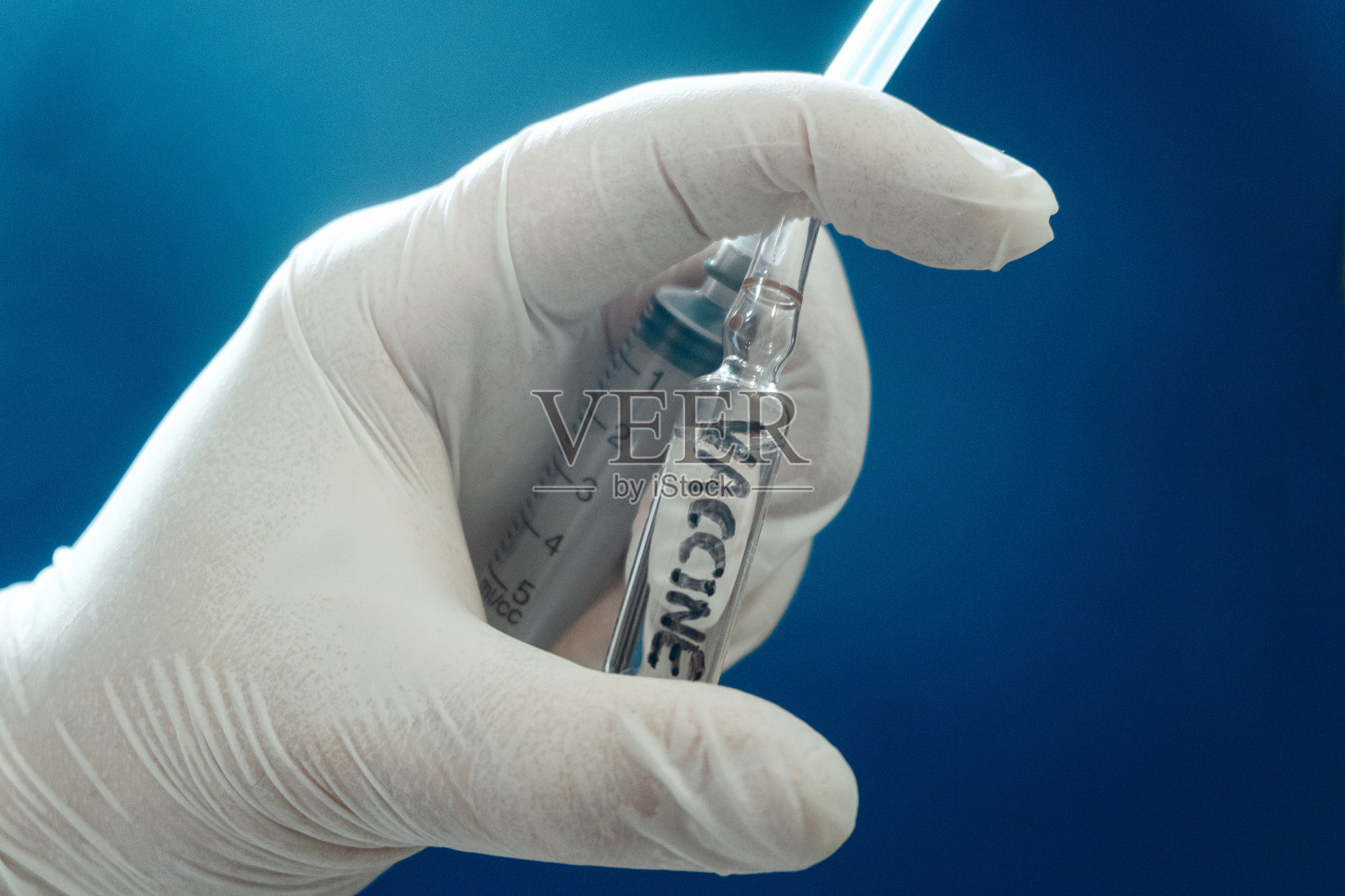 带疫苗的安瓿和医用一次性注射器。医生手里拿着注射用的药。蓝色背景。照片摄影图片