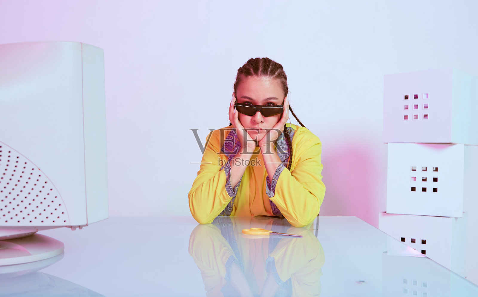 时尚周到的亚洲女性办公室工作人员戴着太阳镜坐在过时的电脑。彩色的霓虹灯照片摄影图片