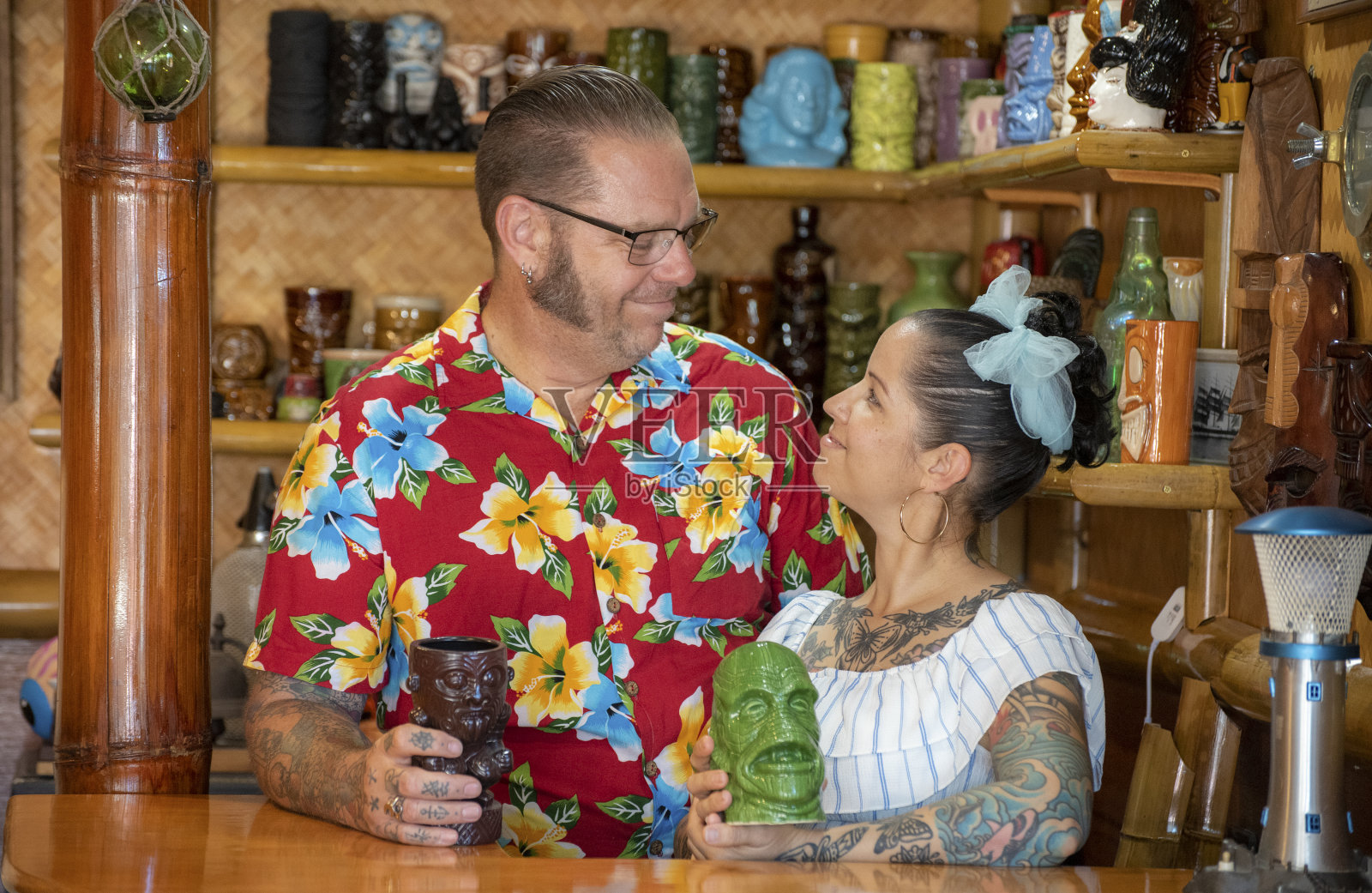 生活在20世纪50年代的一对夫妇…衣服和房子，享受时间在他们的提基酒吧。照片摄影图片