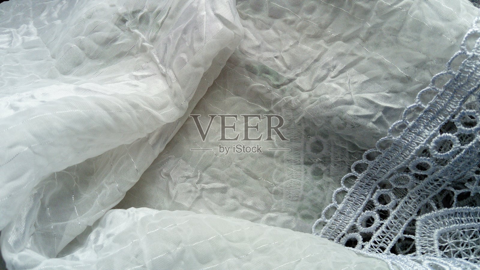 透明的白色合成纤维，有闪亮的白色条纹。无色的薄纱掩盖了房间的舒适度。轻皱的窗帘上有飞扬的粗条纹，缎带和黎塞留的辫子照片摄影图片