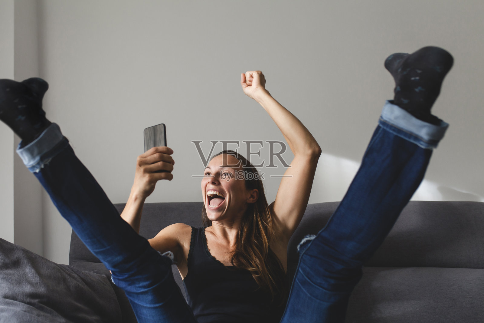 坐在沙发上的白人女子对手机通知反应激动。照片摄影图片