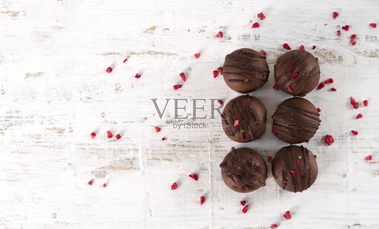 自制美味的巧克力棕色糖果与升华红覆盆子在白色的木制背景。豆杆。照片摄影图片