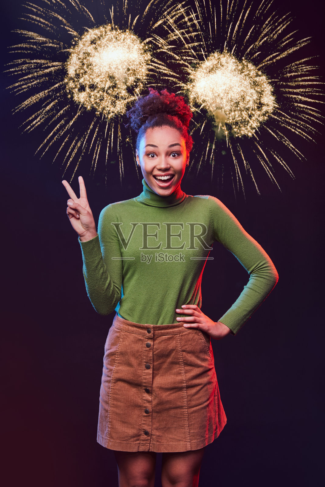 新年或圣诞聚会。垂直拍摄的一个年轻的混合种族妇女显示和平标志和微笑，而站在烟花的背景照片摄影图片