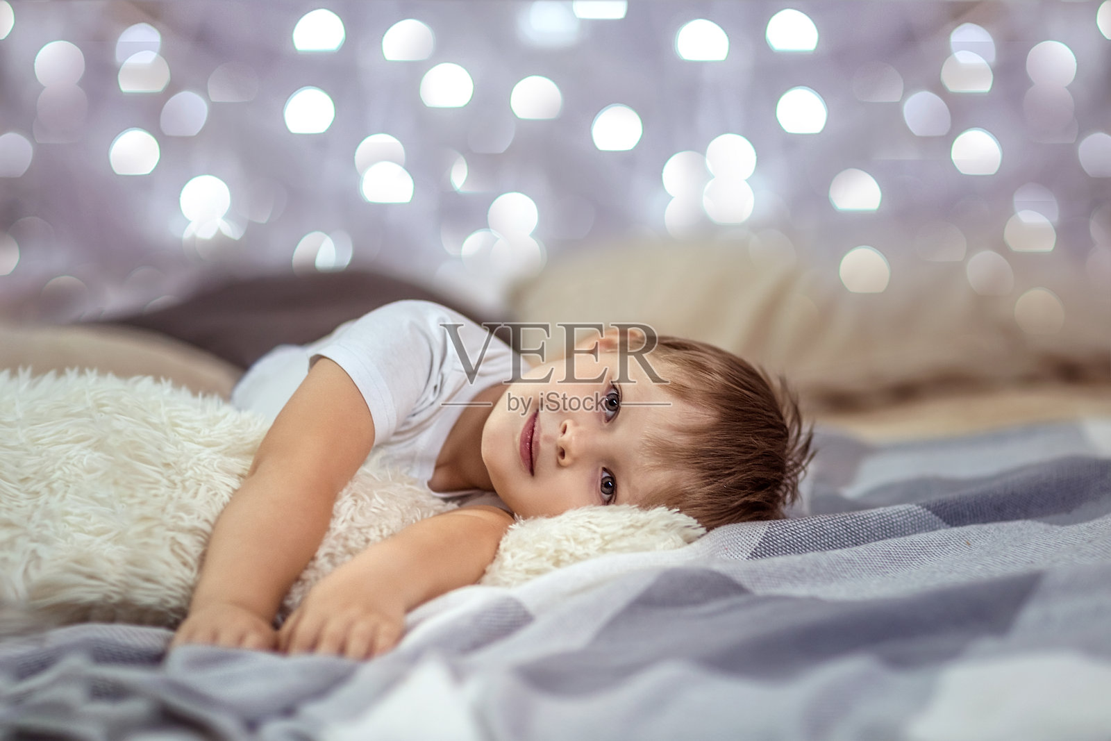 一个4-5岁的漂亮男孩躺在床上，背景是闪闪发光的花环。温馨的圣诞假期家庭气氛。照片摄影图片