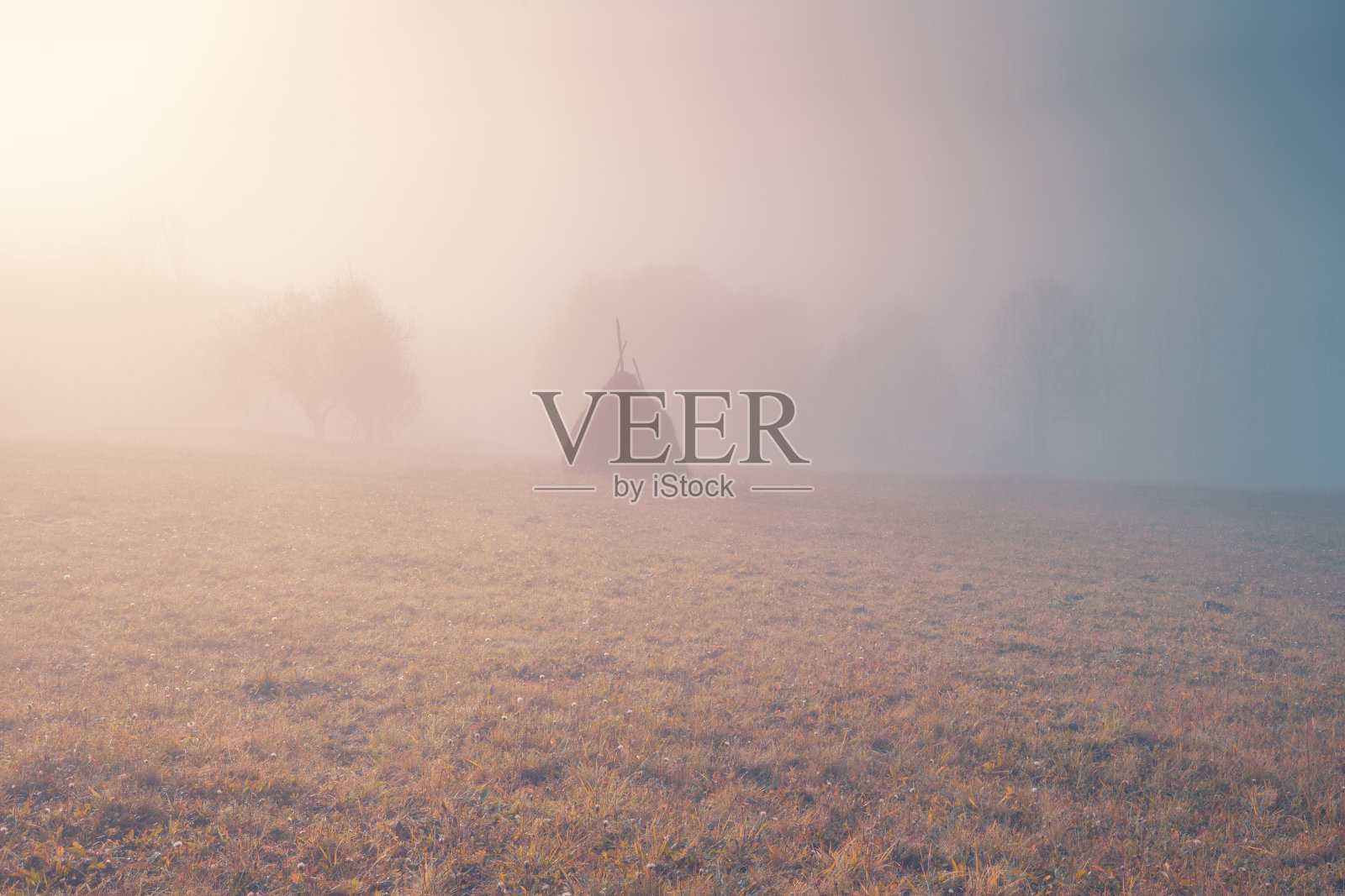 美丽的早晨在多雾的小山。美丽的风景与太阳，从喀尔巴阡山脉升起。农村草原山丘上的草堆和树木。照片摄影图片