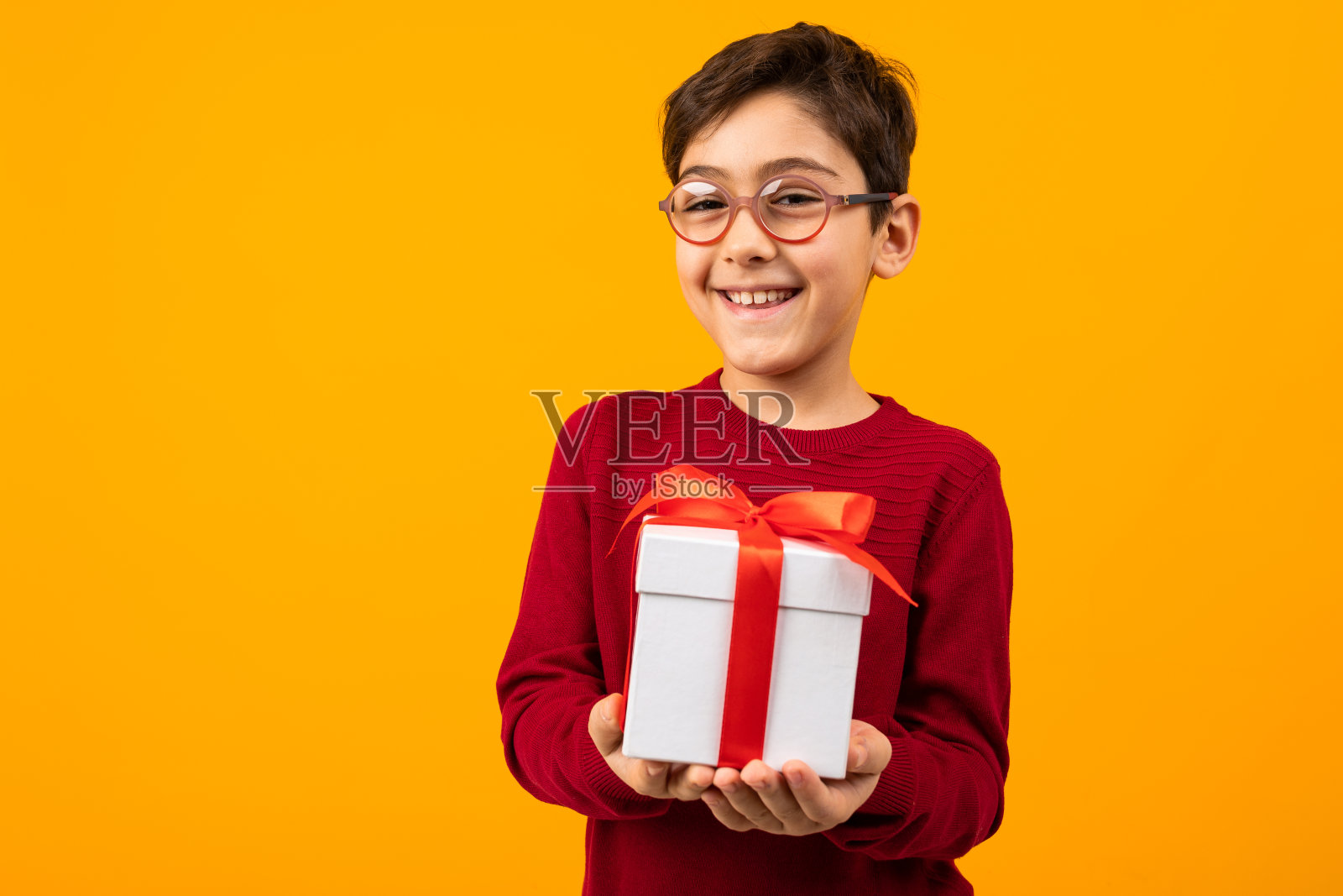 微笑的白人男孩在红色套头衫与一个礼物盒在黄色背景与复制空间照片摄影图片