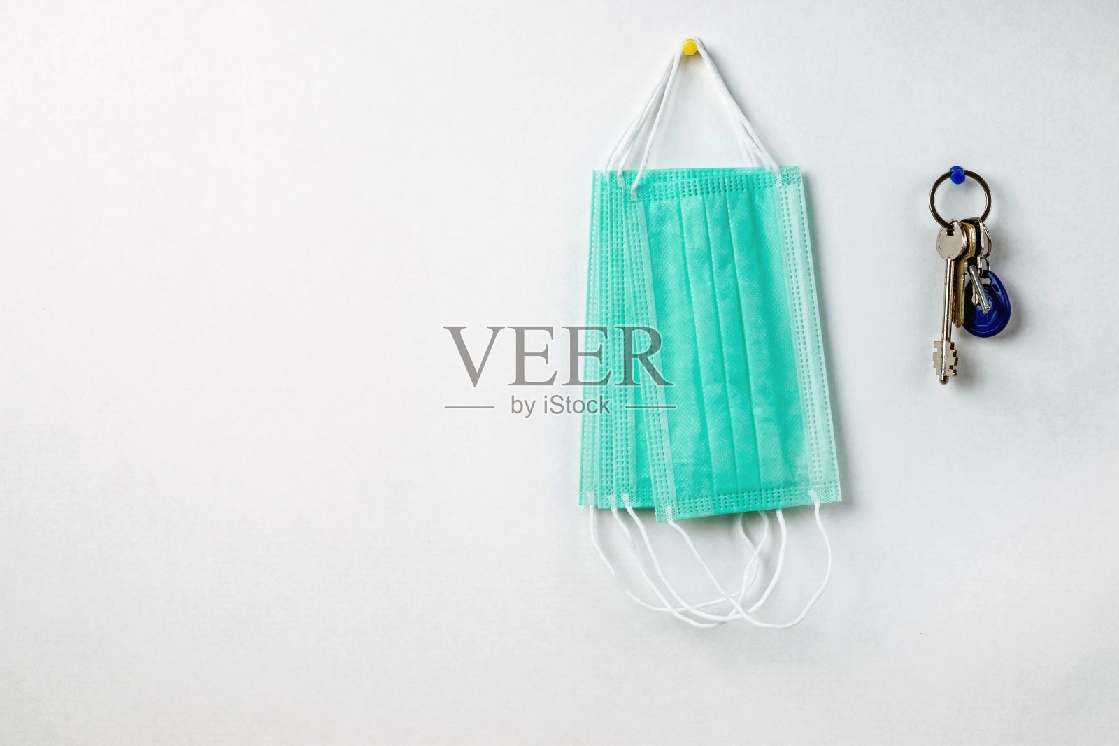 在一堵白墙的背景下，从门锁上摘下绿色医用防护口罩和一串钥匙。照片摄影图片