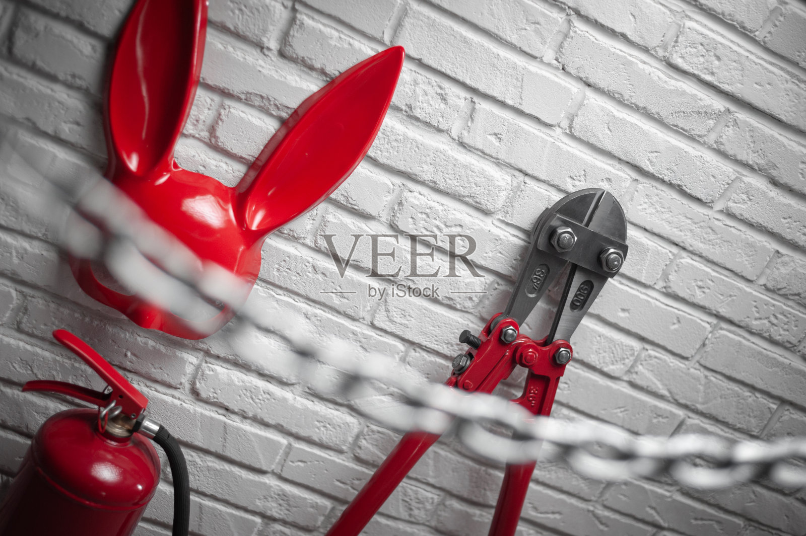 创意设计了带有兔子面具的防火砖墙，灭火器和带有拉伸链的断线钳照片摄影图片