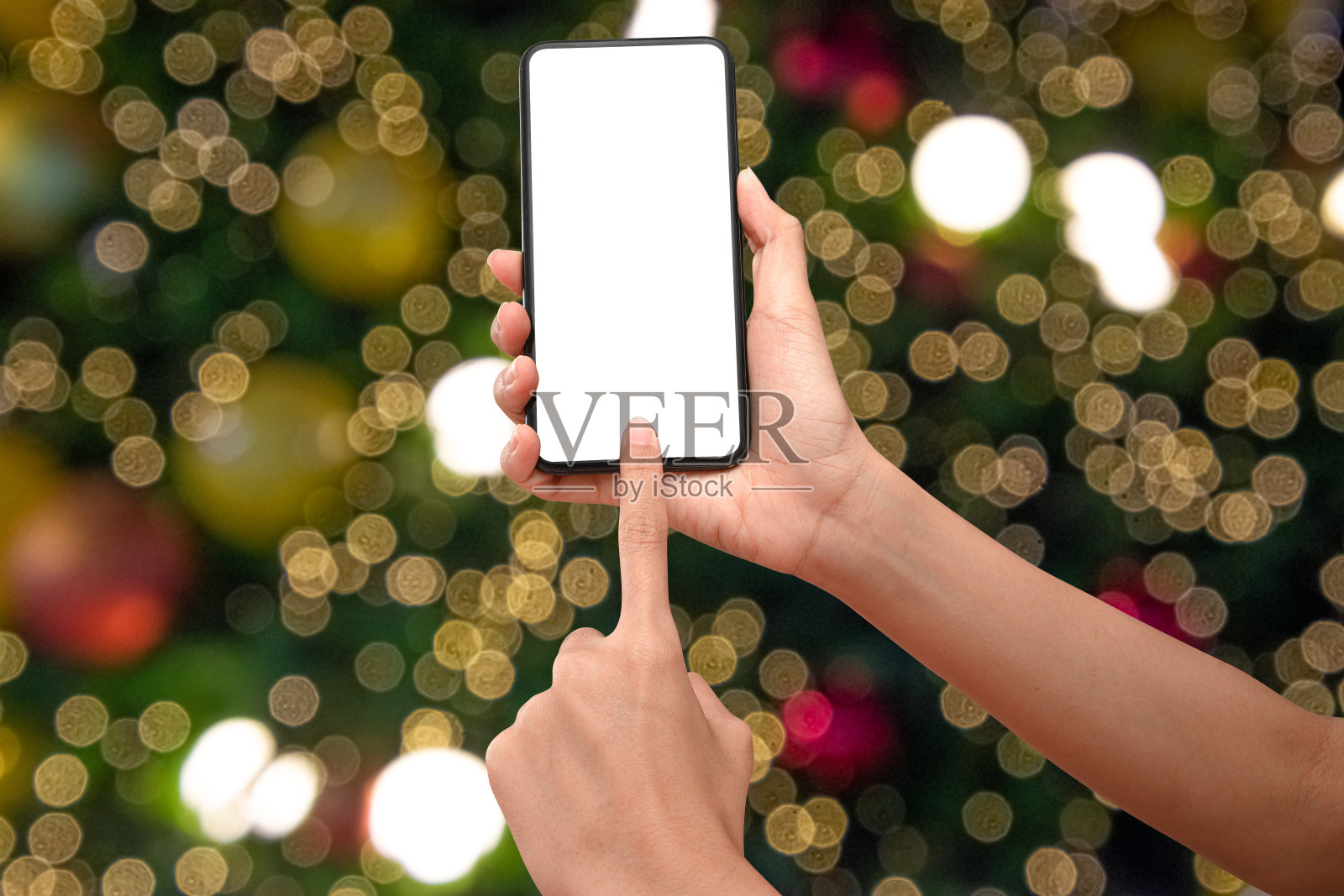 近距离手持手机孤立在白色背景与照明模糊的散景圣诞树装饰与悬挂灯球。照片摄影图片