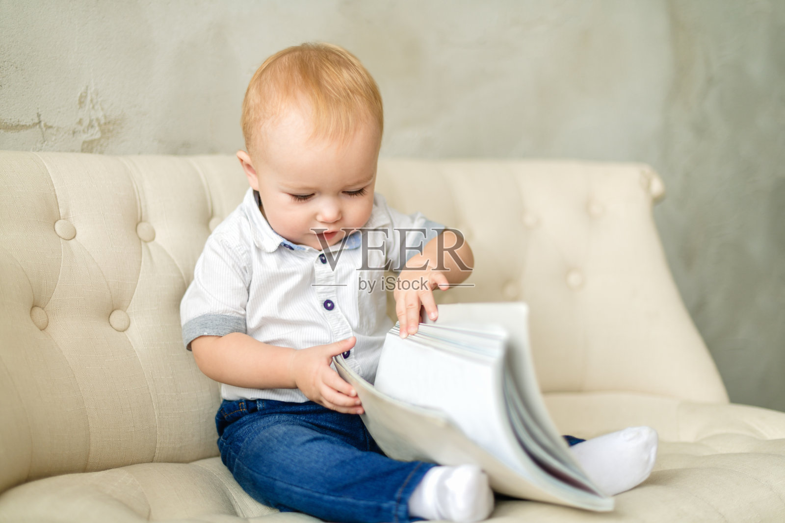 胖乎乎的金发小男孩坐在轻便沙发上看书。一个穿着蓝色牛仔裤和白色衬衫的红头发男孩正在看一本合上的书。摄影水平照片摄影图片