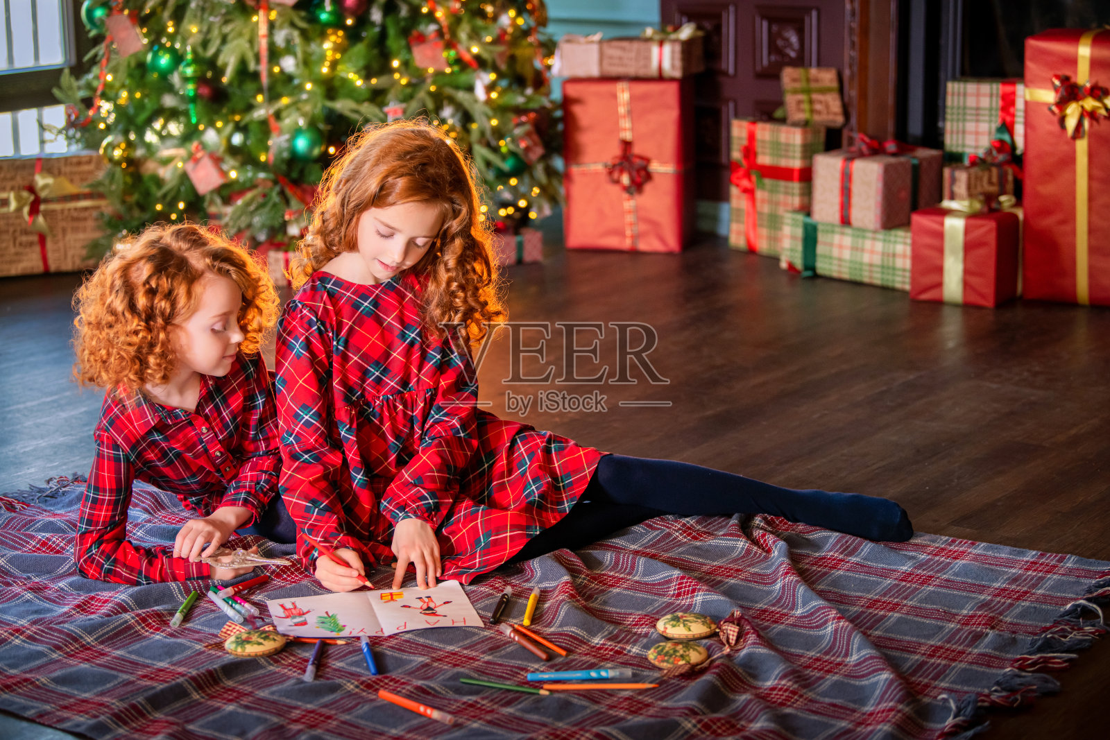 在圣诞树和装饰过的房间里，两个红头发的卷发女孩在给圣诞老人写信。照片摄影图片