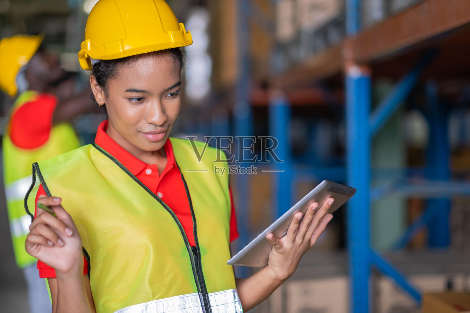 女工在汽车零部件仓库配货中心用药片检查货物。女工程师戴安全帽，穿背心。背景架子上有货物照片摄影图片