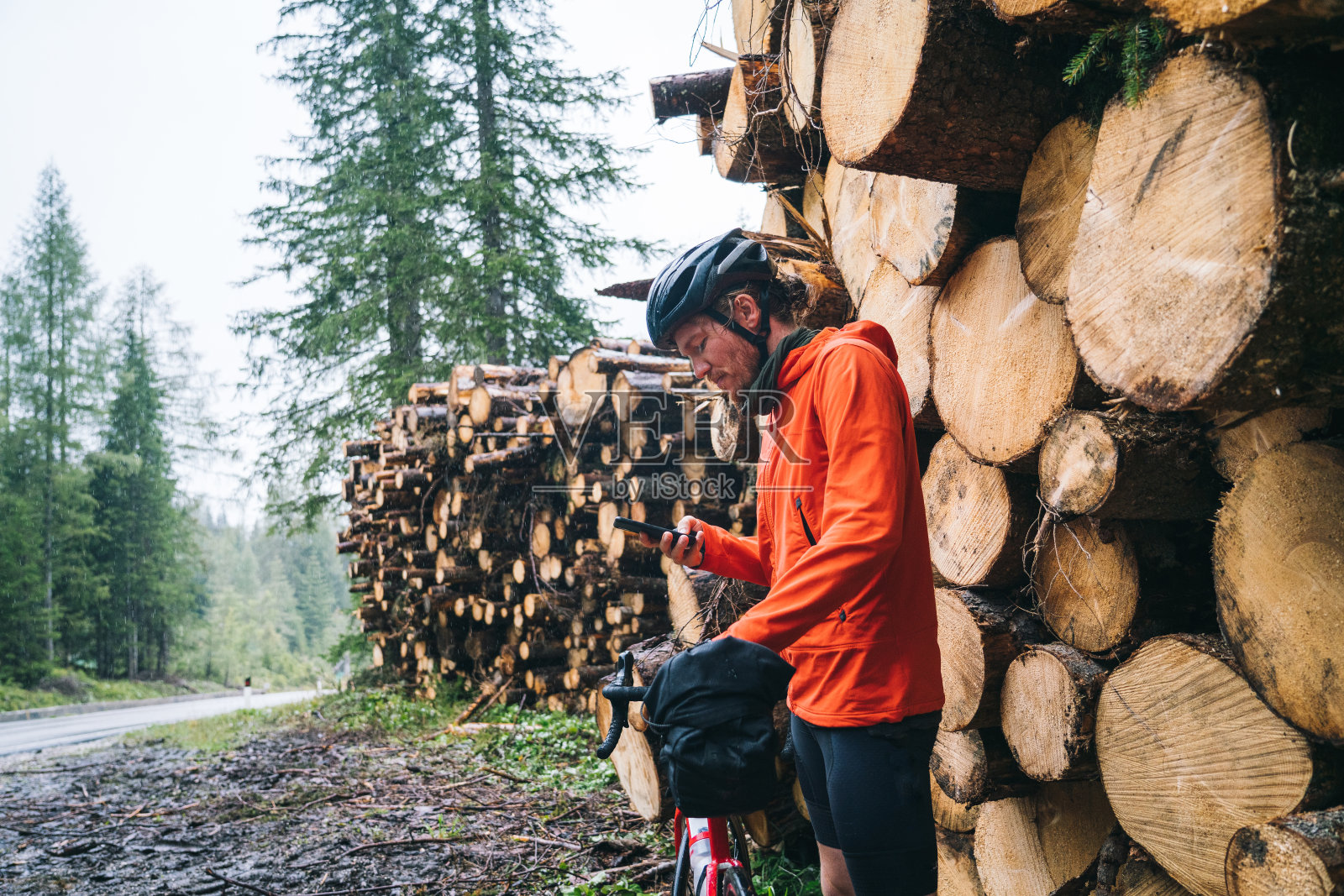 在雨中骑公路自行车的人站在圆木堆旁边照片摄影图片