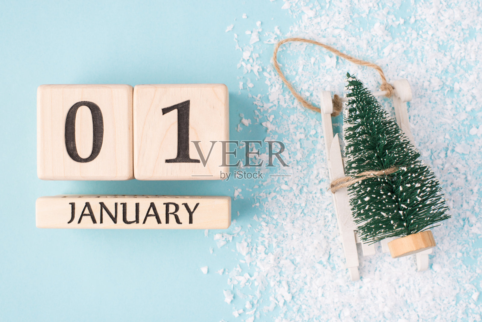 新年是这里的概念。顶部上方俯瞰照片的木立方体显示的第一天的一年和小圣诞树在雪橇上孤立的浅蓝色背景与雪照片摄影图片