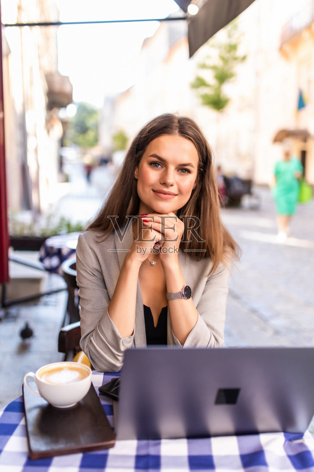 微笑的年轻女子与笔记本电脑坐在街头咖啡馆，浏览网页和社交网络饲料，与朋友发短信照片摄影图片