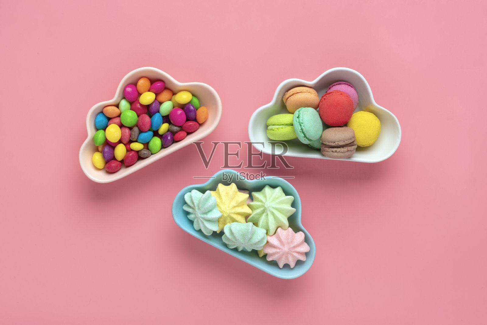 五彩缤纷的糖果-棒棒糖，蛋白酥皮，杏仁饼干在碗状的云孤立在粉红色的背景平lay顶视图小山不健康和美味的食物创意概念节日贺卡照片摄影图片