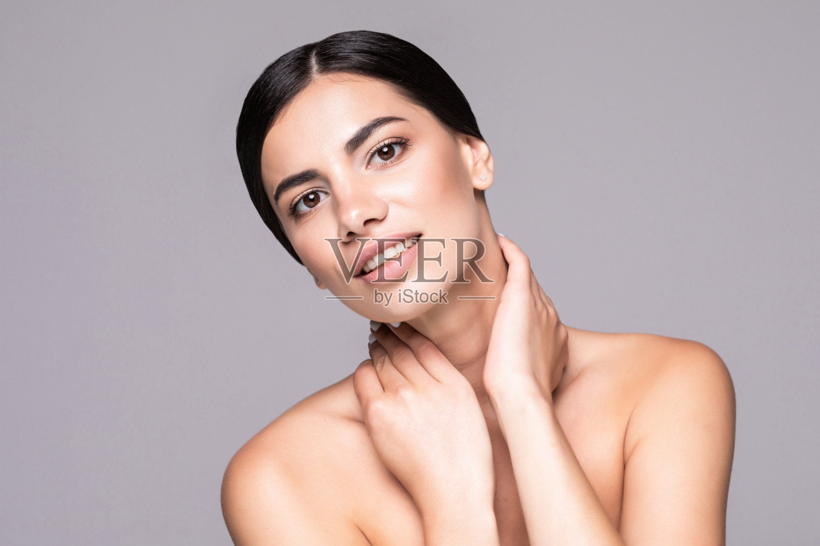 年轻女子淡妆，固定头发后，大眼睛和裸露的肩膀在灰色的工作室背景照片摄影图片