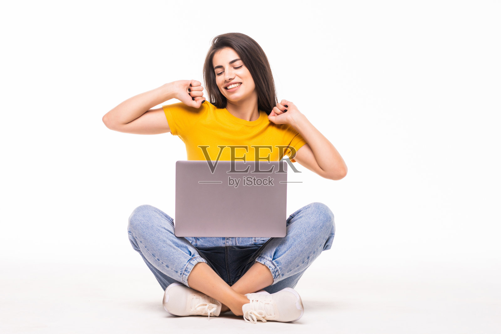 年轻女子坐在地板上，手举着笔记本电脑，孤立地坐在白色背景上照片摄影图片