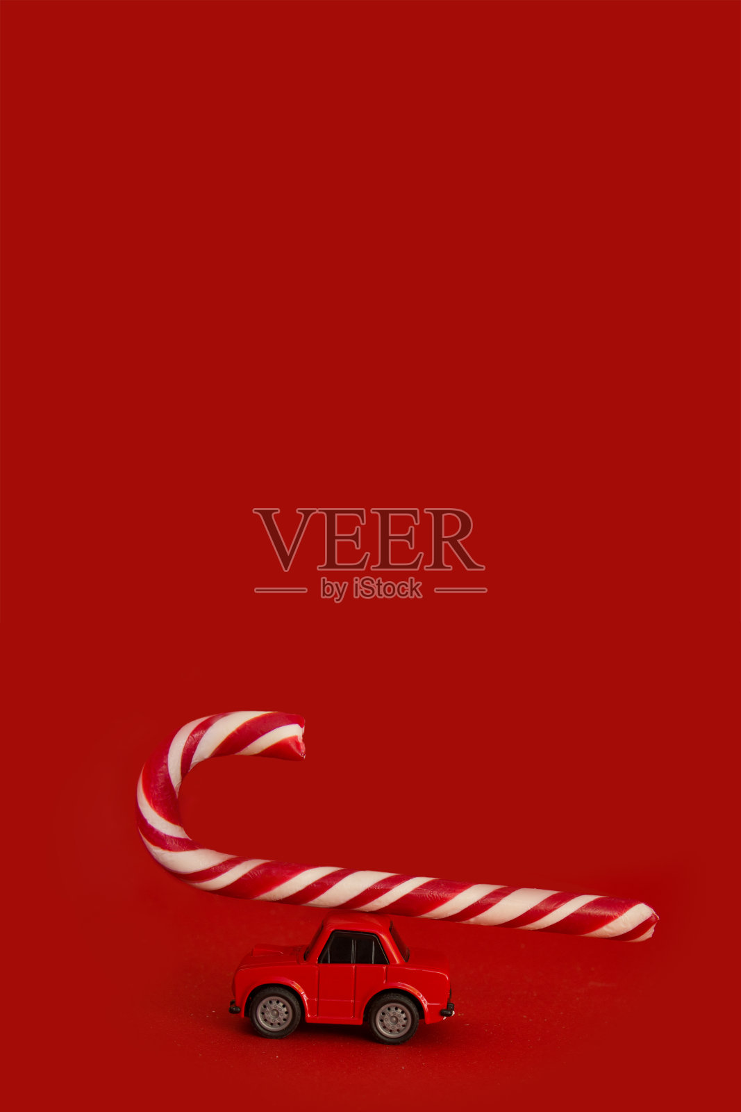 圣诞布局的红色背景与地方的文字。红色的玩具汽车模型与新年的糖果手杖。薄荷棒棒糖。垂直格式。Copyspace照片摄影图片