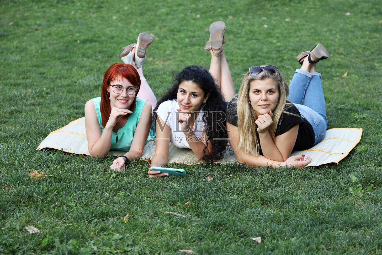 三个年轻的女孩微笑着躺在草地上的毯子上看着镜头照片摄影图片