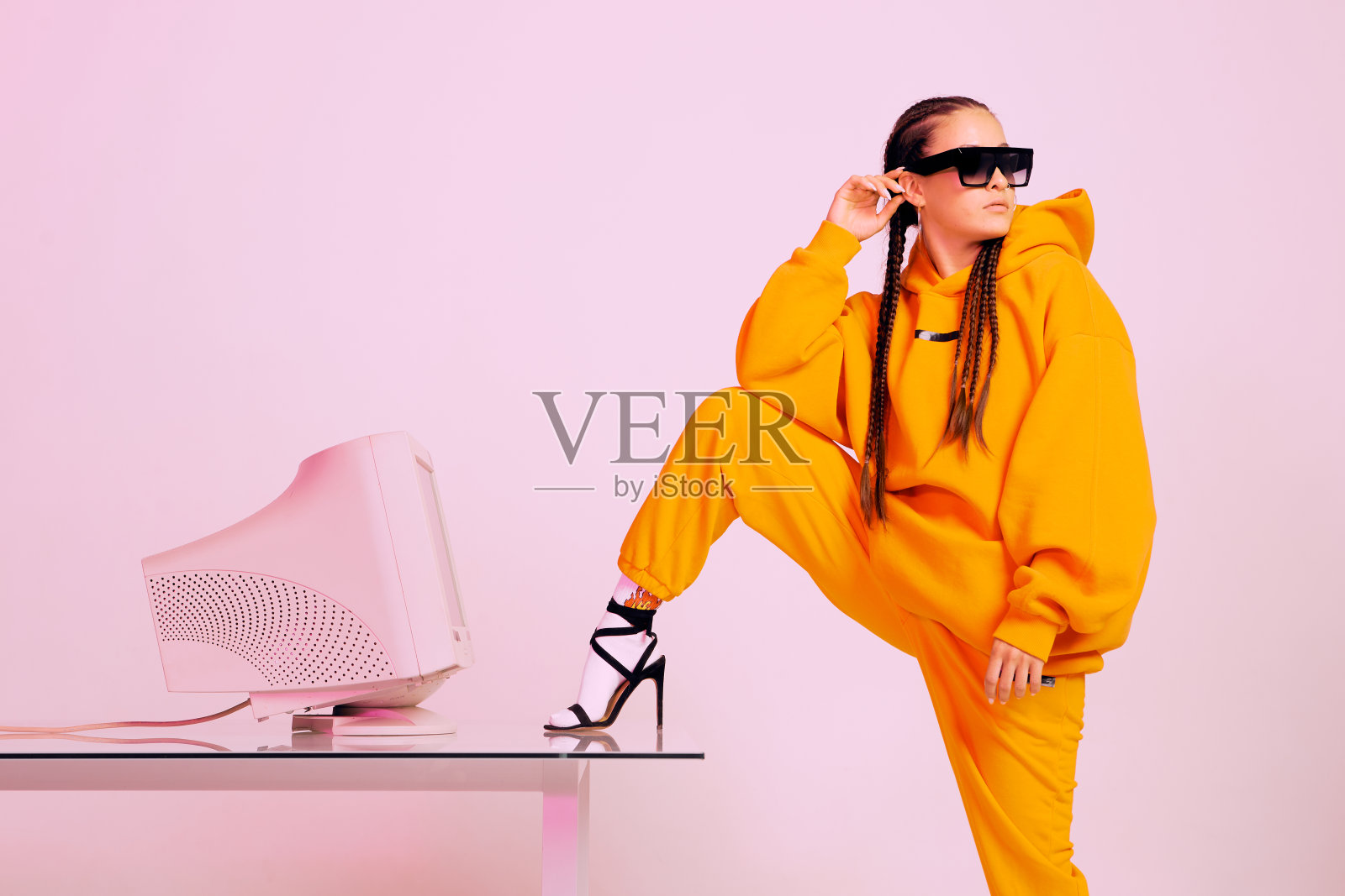 时髦的年轻女性办公室职员太阳镜和过时的电脑和脚在桌子上。彩色霓虹灯照片摄影图片